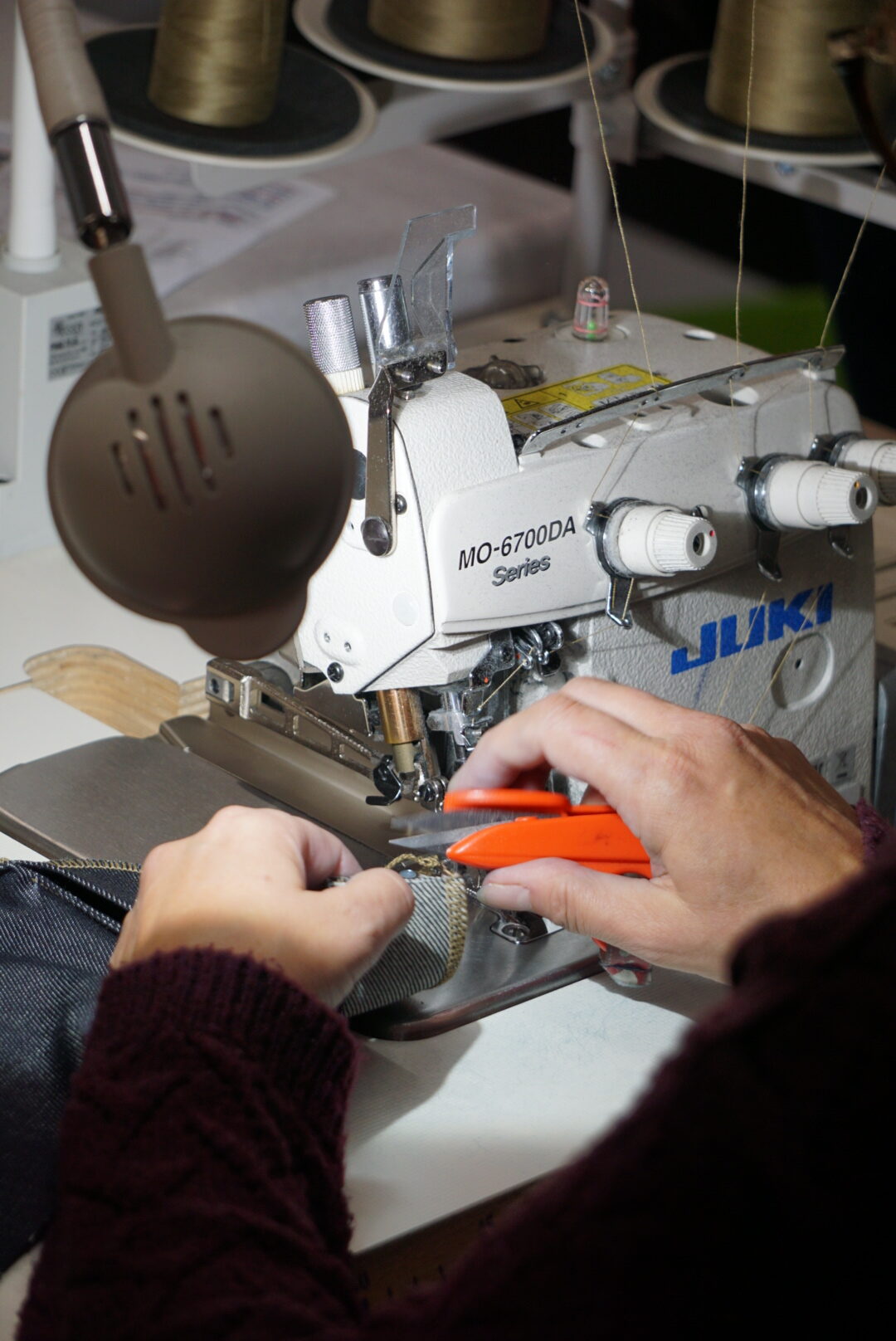 Les mains expertes de nos couturières découpant le surplus de toile denim sur une surjeteuse industrielle JUKI, garantissant la qualité de fabrication Kiplay Vintage.